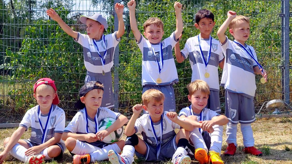 Group of young soccer players posing with medals after a match, some raising their arms in celebration