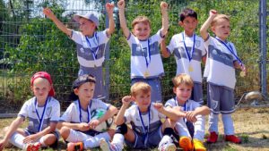 Group of young soccer players posing with medals after a match, some raising their arms in celebration