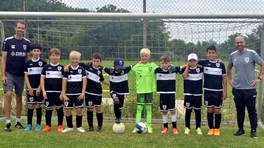 Youth soccer team lined up with two coaches on a grassy field in front of a goalpost.
