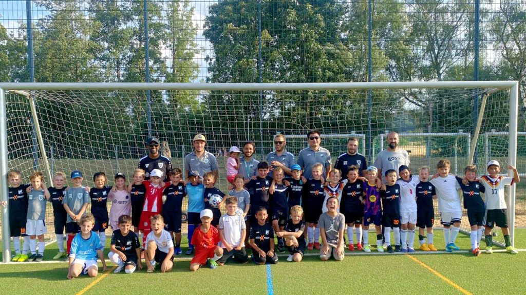 Group of young soccer players and coaches posing for a photo in front of a goal on a sunny field.