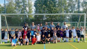Group of young soccer players and coaches posing for a photo in front of a goal on a sunny field.