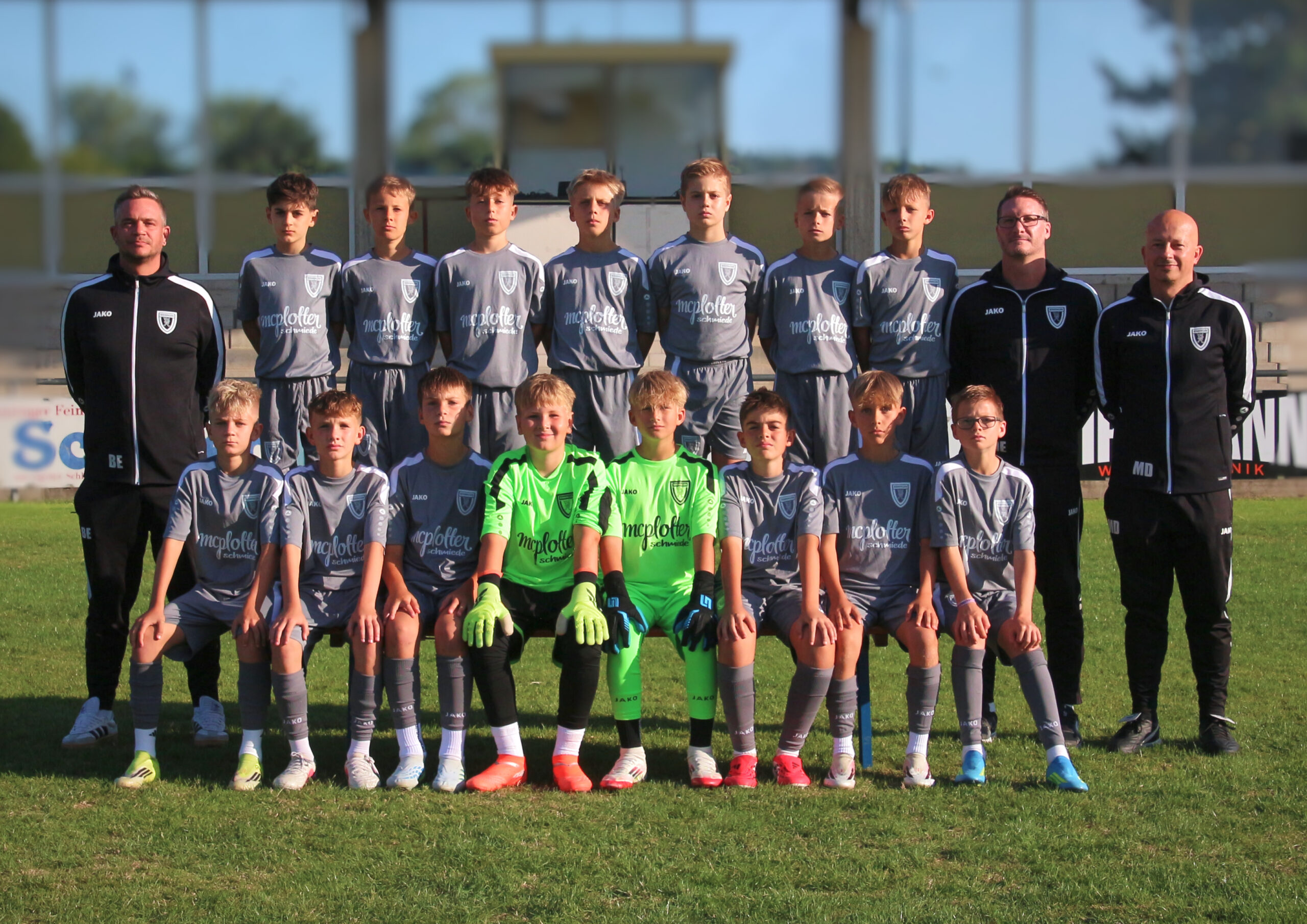 Youth soccer team and coaches posing for a group photo on a grassy field at the stadium edge.