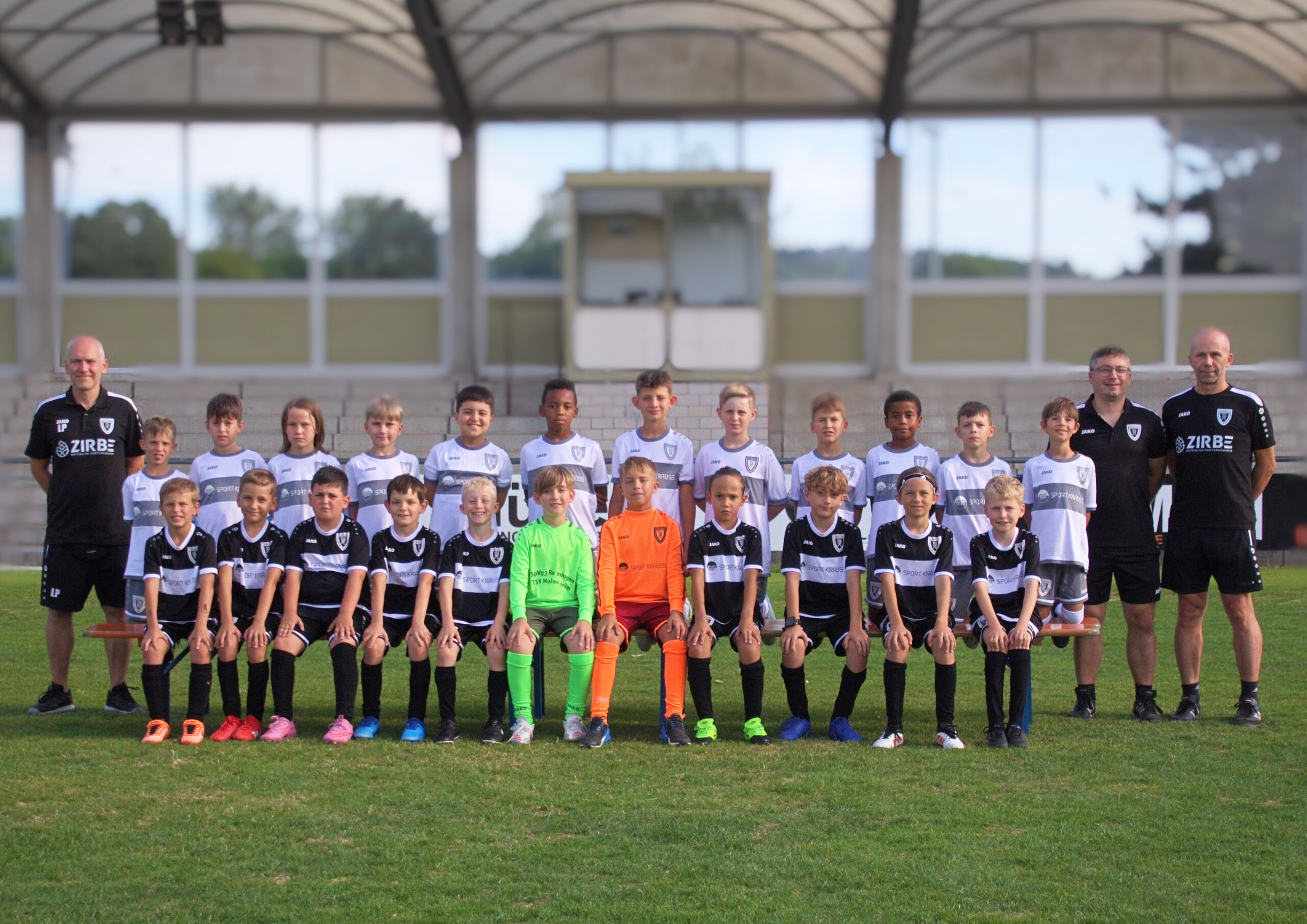 Youth soccer team posing for a group photo on a grass field with two coaches at the ends.